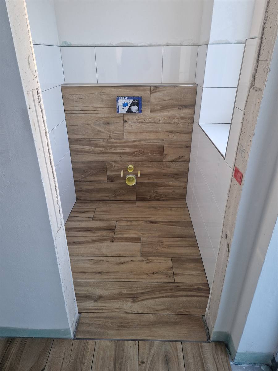 Gäste-WC im Rohbauzustand: Wand bereits gefliest, Anschlüsse für das wandhängende WC noch mit gelben Kappen verschlossen